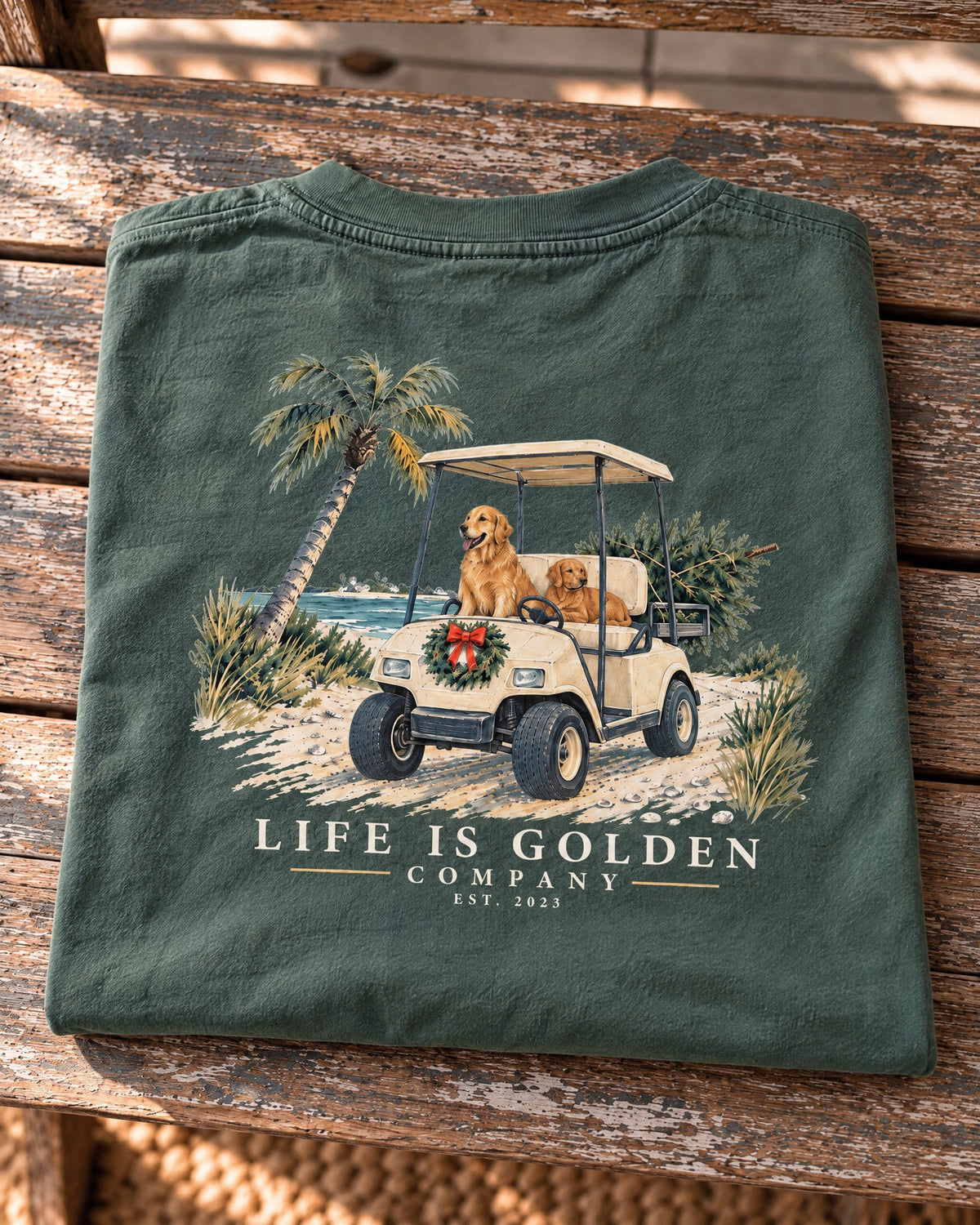 Coastal Christmas Ride heavyweight tee folded flat on a navy sweatshirt on the horizontal wooden bench seat, with the full back artwork visible.