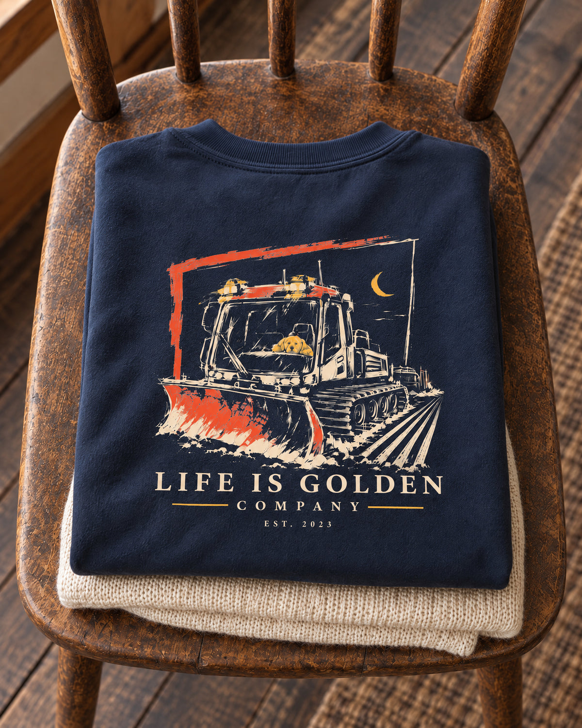 Navy Corduroy Crew crewneck folded flat on an ivory knit on a wooden chair seat, with full back artwork visible.