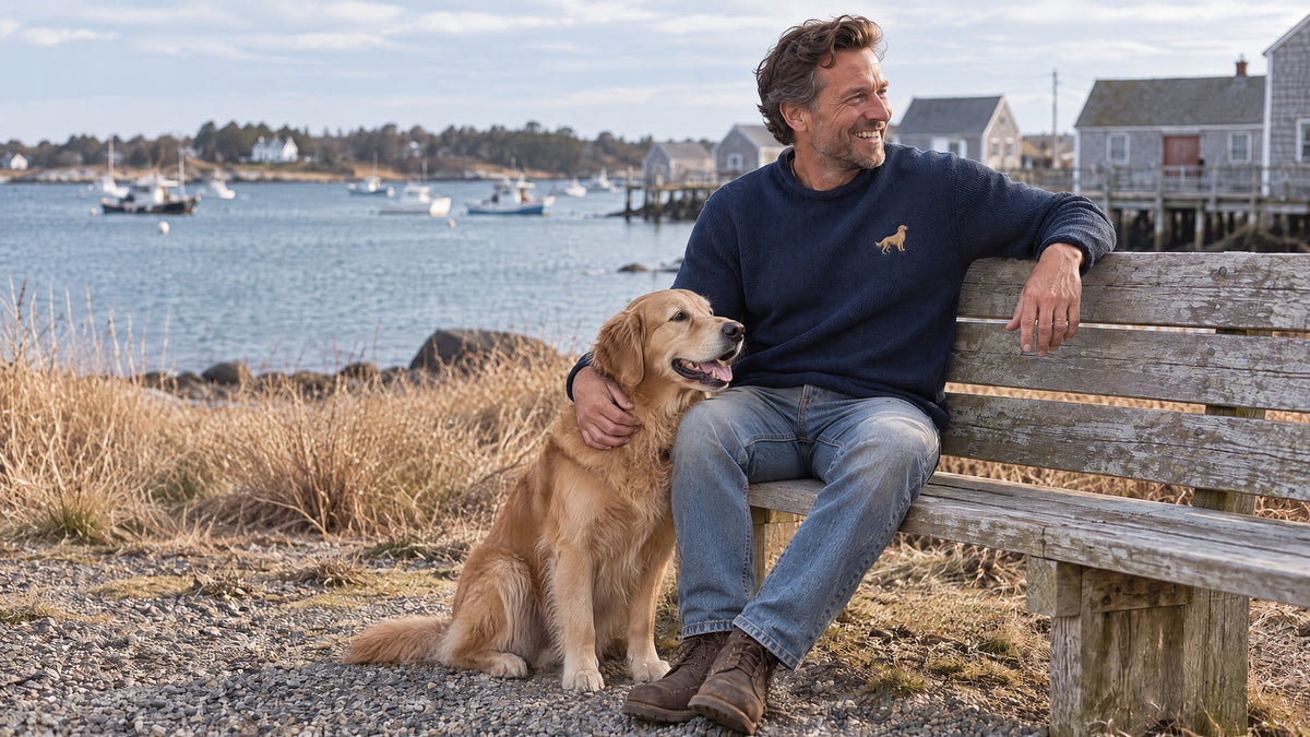 The navy Golden Wellfleet roll neck worn by a man relaxing on a weathered harbor bench.