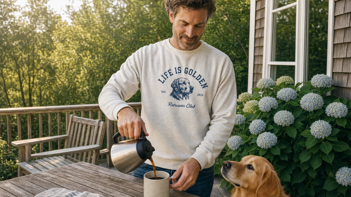 a hydrangea-lined back porch in cool september morning light, a man facing forward pouring coffee while his golden retriever waits beside him