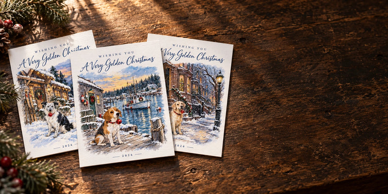 Personalized Christmas cards with painted dog scenes, photographed on a wooden table beside winter greenery